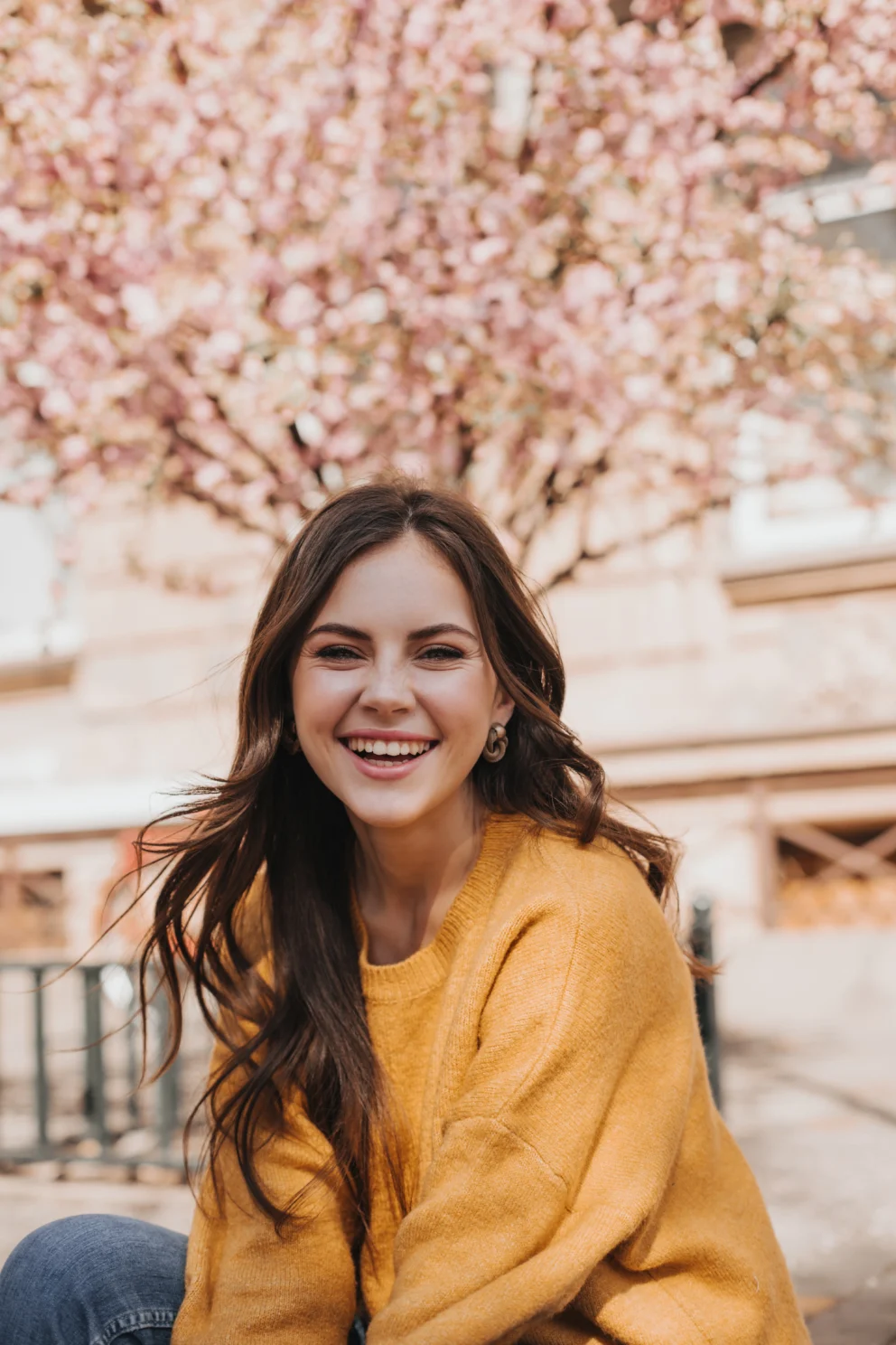 cheerful-girl-cashmere-sweater-laughs-against-backdrop-blossoming-sakura-portrait-woman-yellow-hoodie-city-spring